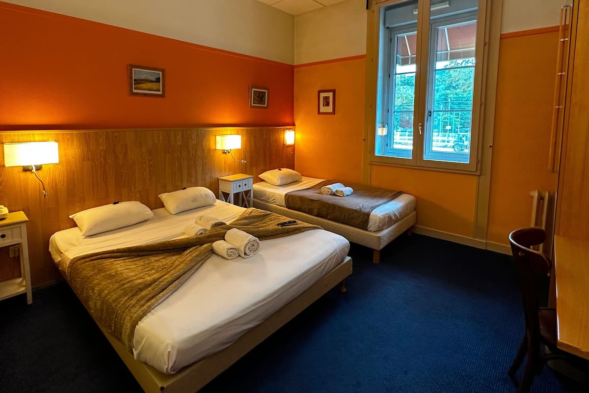 Ein Hotelzimmer mit zwei Betten, einem Nachttisch, einer Lampe und einem Fenster mit Blick ins Freie.