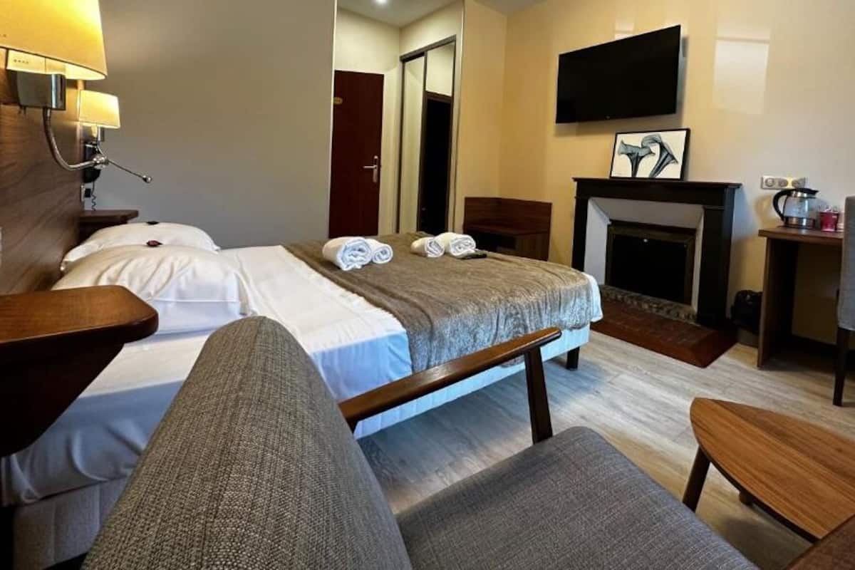 Ein Hotelzimmer mit Bett, Sessel, kleinem Tisch, Kamin und Wandfernseher.