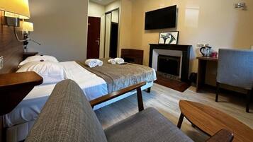 A hotel room with a bed, a chair, a small table, a fireplace, and a TV mounted on the wall.