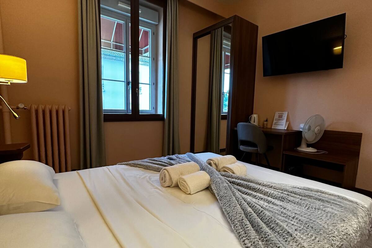 Ein Hotelzimmer mit Bett, Schreibtisch, Stuhl, Fernseher und einem Fenster mit Vorhängen.
