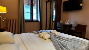 Ein Hotelzimmer mit Bett, Schreibtisch, Stuhl, Fernseher und einem Fenster mit Vorhängen.