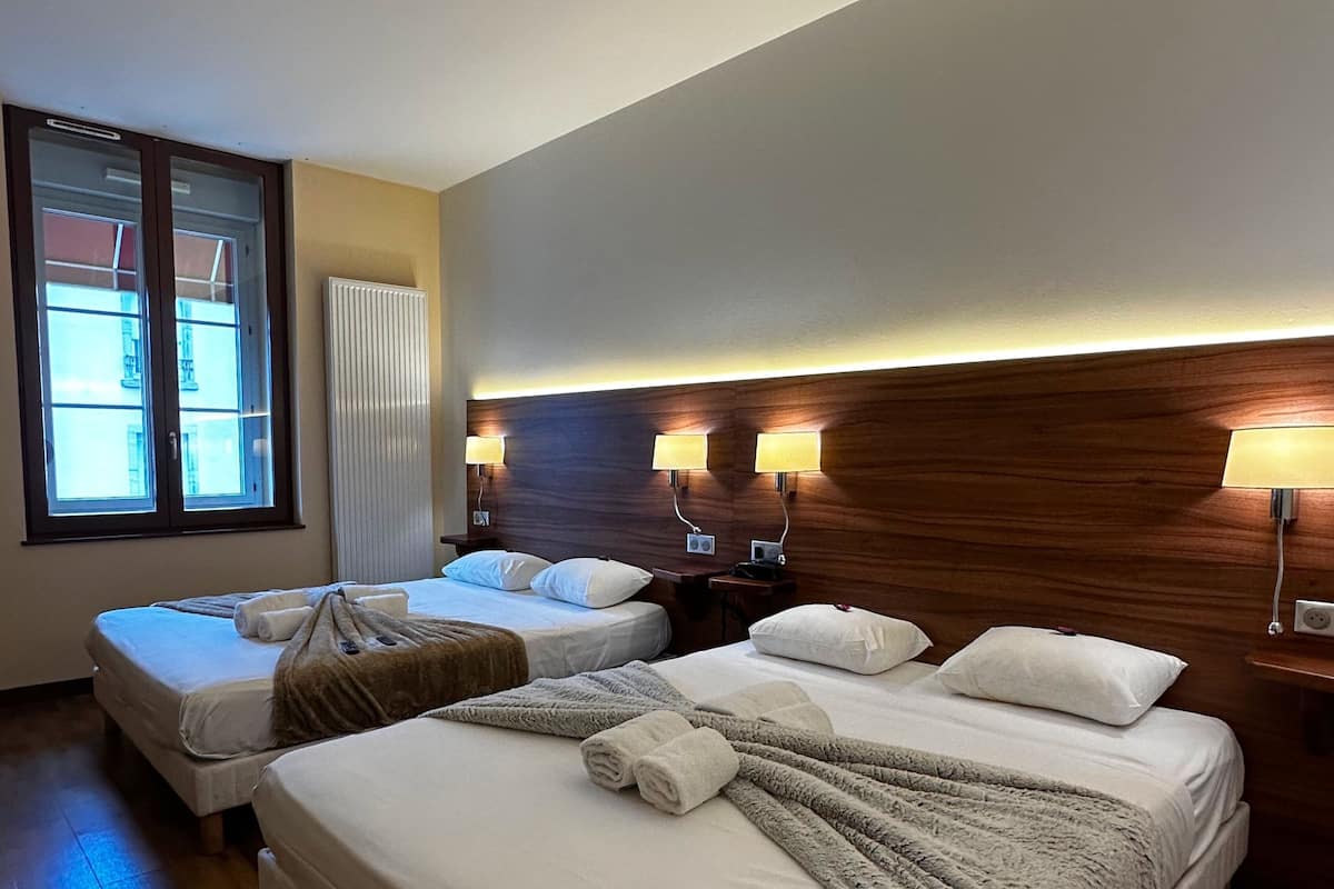 Ein Hotelzimmer mit zwei Betten, einem Holzkopfende, Nachttischlampen und einem Fenster mit Jalousien.