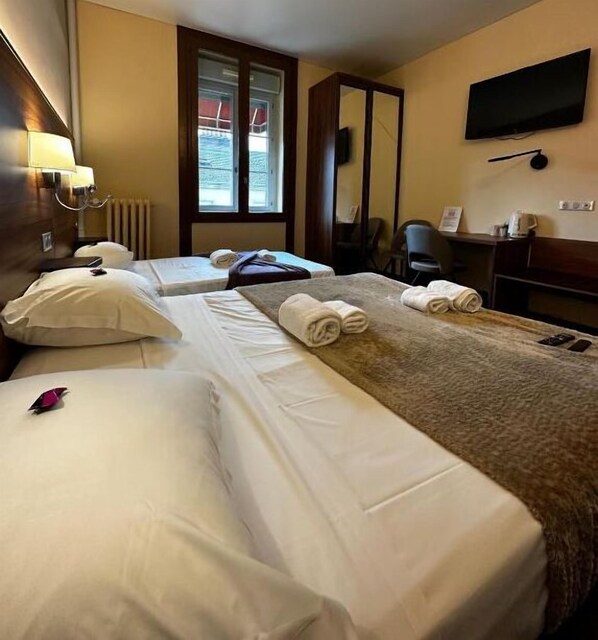 Una habitación de hotel con dos camas, un ventanal amplio, un televisor de pantalla plana y un escritorio con una silla.