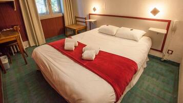 A hotel room with a bed, a desk, a chair, and a telephone.