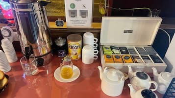 A breakfast setup with a coffee maker, teapot, cups, and a box of assorted tea bags.