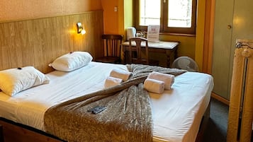 A hotel room with a large bed, a desk, and a window.