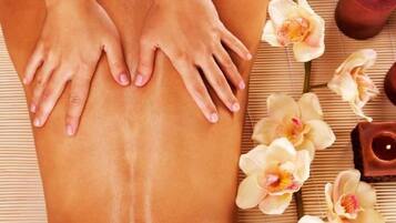 Iemand ontvangt een massage, handen op de rug, omringd door bloemen en kaarsen.