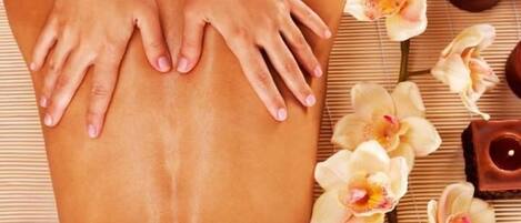 A person receiving a massage with hands on their back, surrounded by flowers and candles.