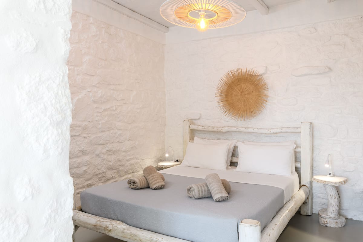 Un lit avec une tête de lit blanche, un luminaire fixé au mur et une petite table de chevet avec une lampe.