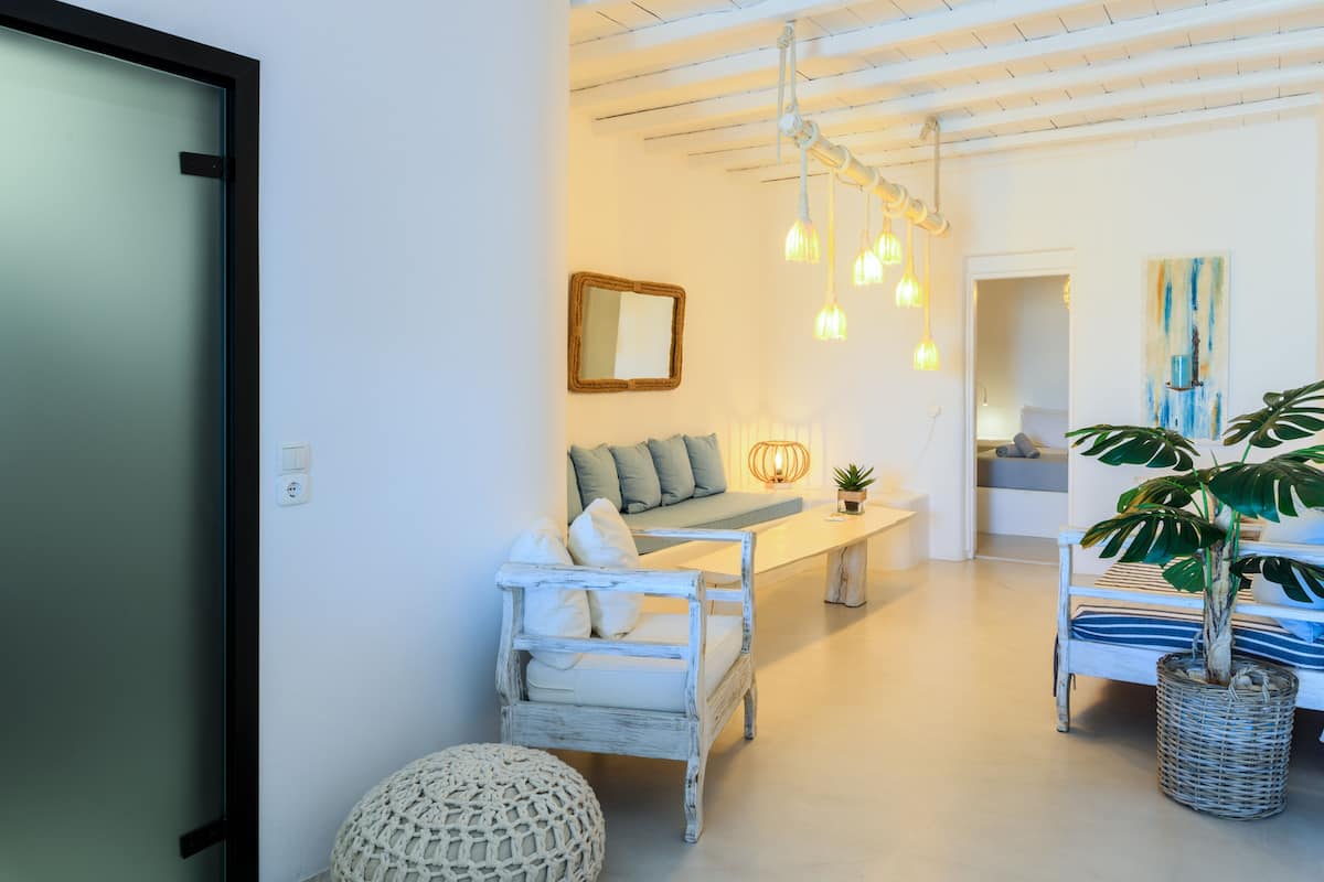 Un salon moderne avec un canapé blanc, une chaise en bois et un banc. On y trouve des luminaires suspendus, un miroir et une plante.