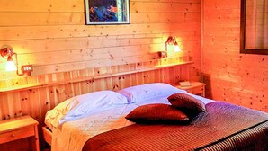 En stuga med träpanel, ett rum med en säng, två sänglampor och en inramad tavla på väggen.