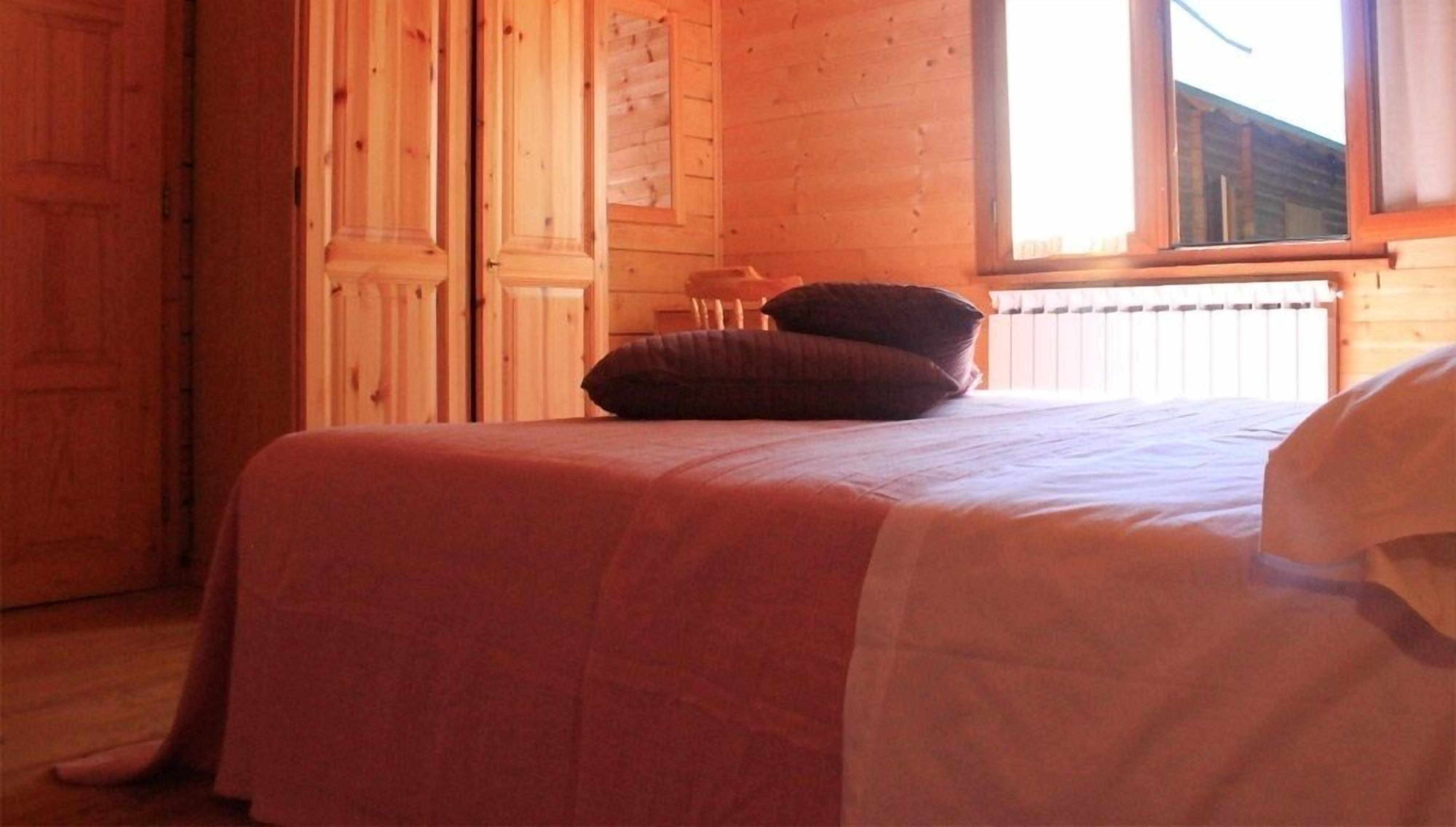 Una stanza in legno con un letto, una finestra e un termosifone.