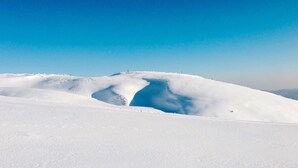 Ett snötäckt landskap med en stor, snötäckt kulle och en tydligt synlig blå vattenyta.