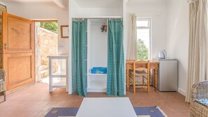 A compact room with a white door, a small table, a chair, a refrigerator, and a window with curtains. - Modern Beach Appartment (Cape Town)
