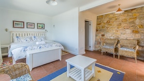 A bedroom with a bed, two wicker chairs, a small white table, and a stone wall. - Modern Beach Appartment (Cape Town)