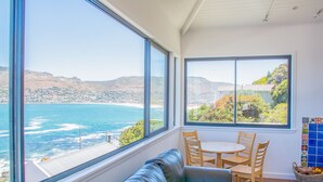 A room with a large window overlooking a coastal view, a blue leather sofa, and a small round table with chairs. - Modern Beach Appartment (Cape Town)