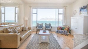 Een woonkamer met een bank, twee fauteuils, een salontafel en uitzicht op zee door grote ramen.