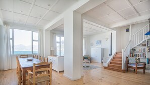 Een ruime woonkamer met een houten eettafel, stoelen, een trap en een boekenkast.