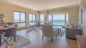 Amplia sala de estar con un ventanal con vista al océano, un comedor con mesa y sillas, y una zona de estar acogedora con un sofá y sillones.