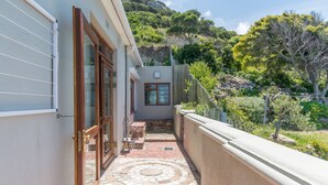 Un estrecho pasillo exterior con un sendero de losas de piedra que conduce a una puerta, rodeado de un muro bajo y follaje.