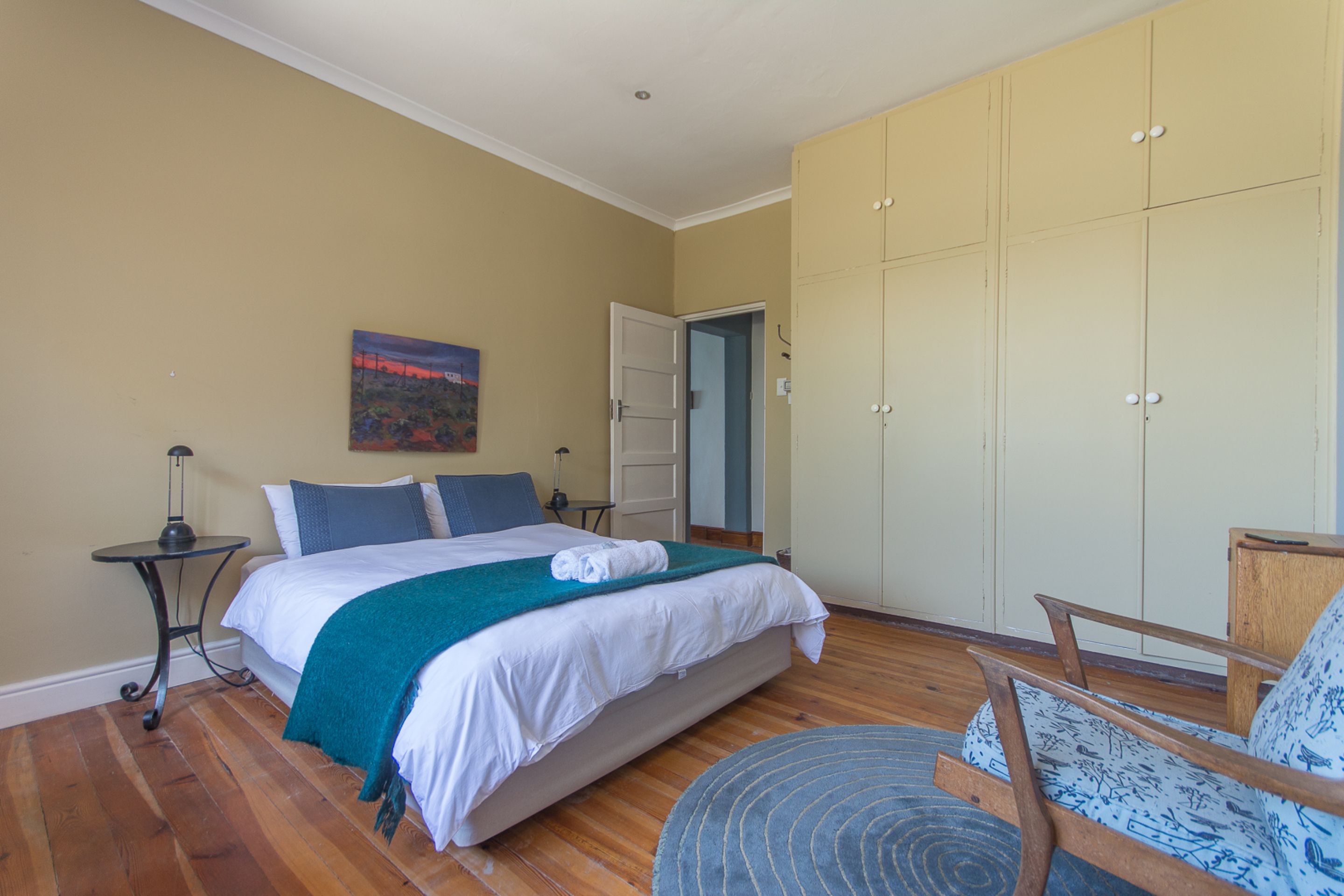 A bedroom with a bed, a chair, a wardrobe, and a painting on the wall.
