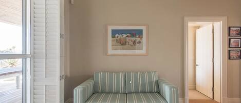 A room with a striped sofa, a painting on the wall, and a door leading to another room.