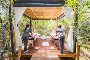 Une terrasse en bois avec deux tables de massage, une table blanche et un luminaire suspendu.
