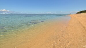 Uma praia com águas cristalinas e rasa, e uma faixa de areia.