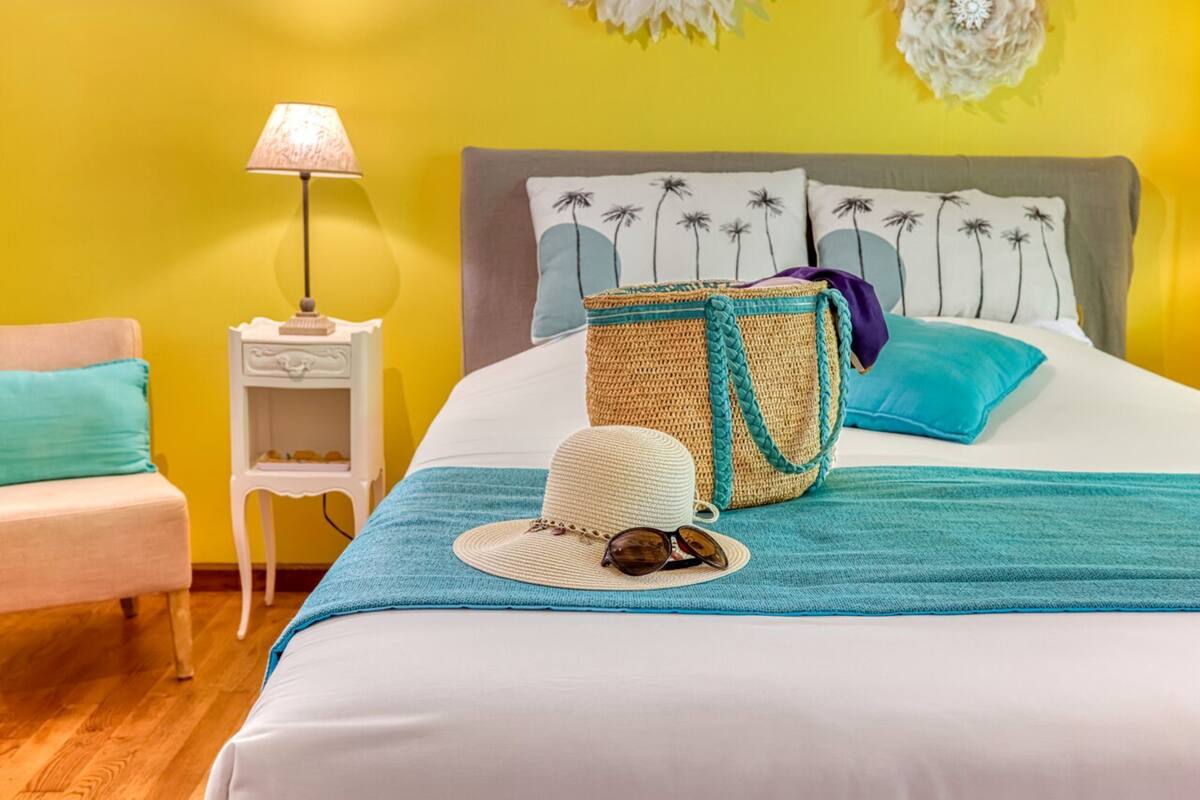 Ein Bett mit einer blau-weißen Streifenbedeckung, einem gewebten Korb, einem Strohhut und Sonnenbrille.