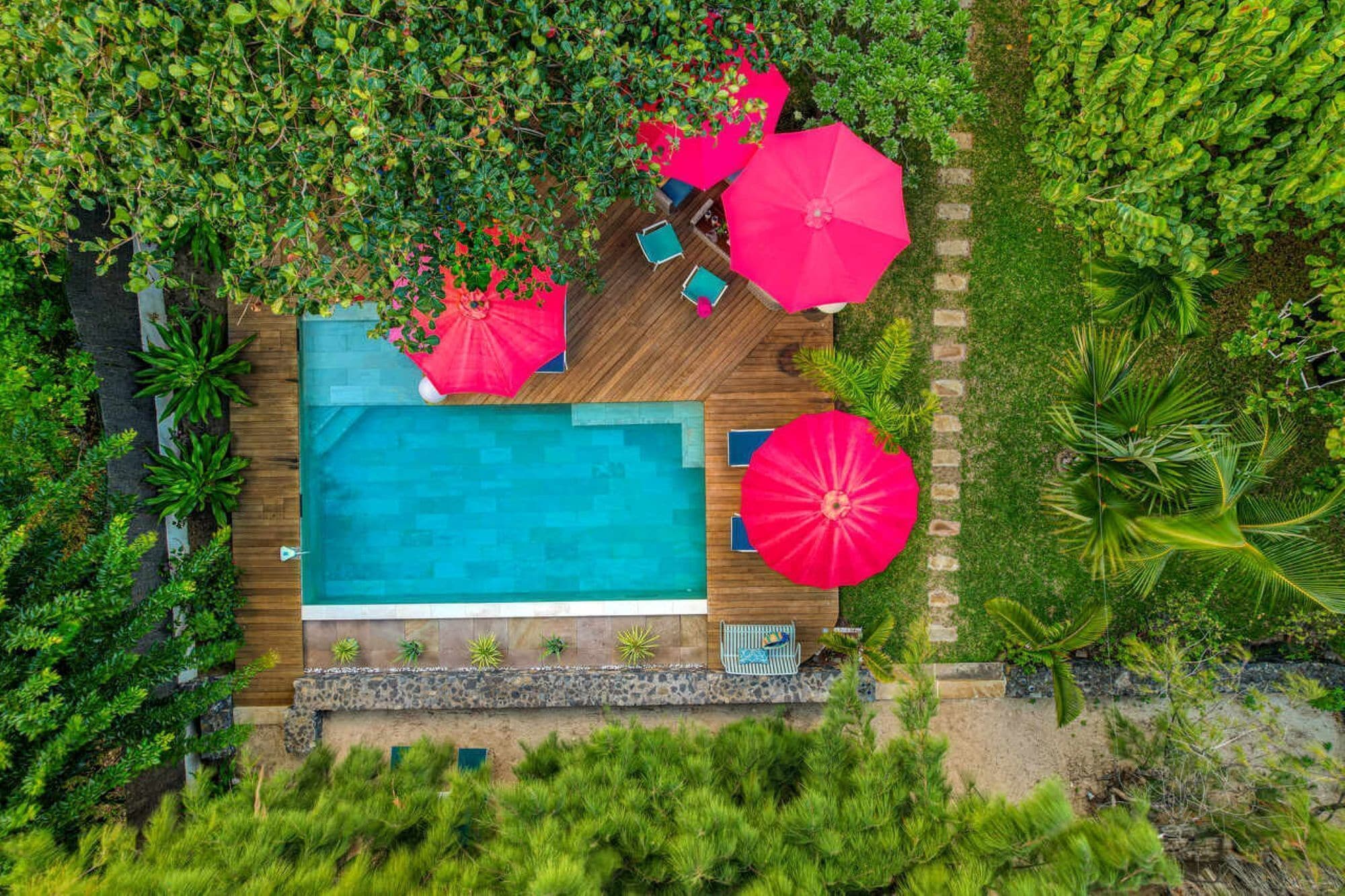 An aerial view of a swimming pool surrounded by lush greenery and red umbrellas.