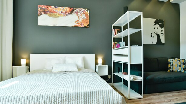Quarto moderno com uma cama grande, uma mesa de cabeceira branca, um aparador branco e um sofá escuro.