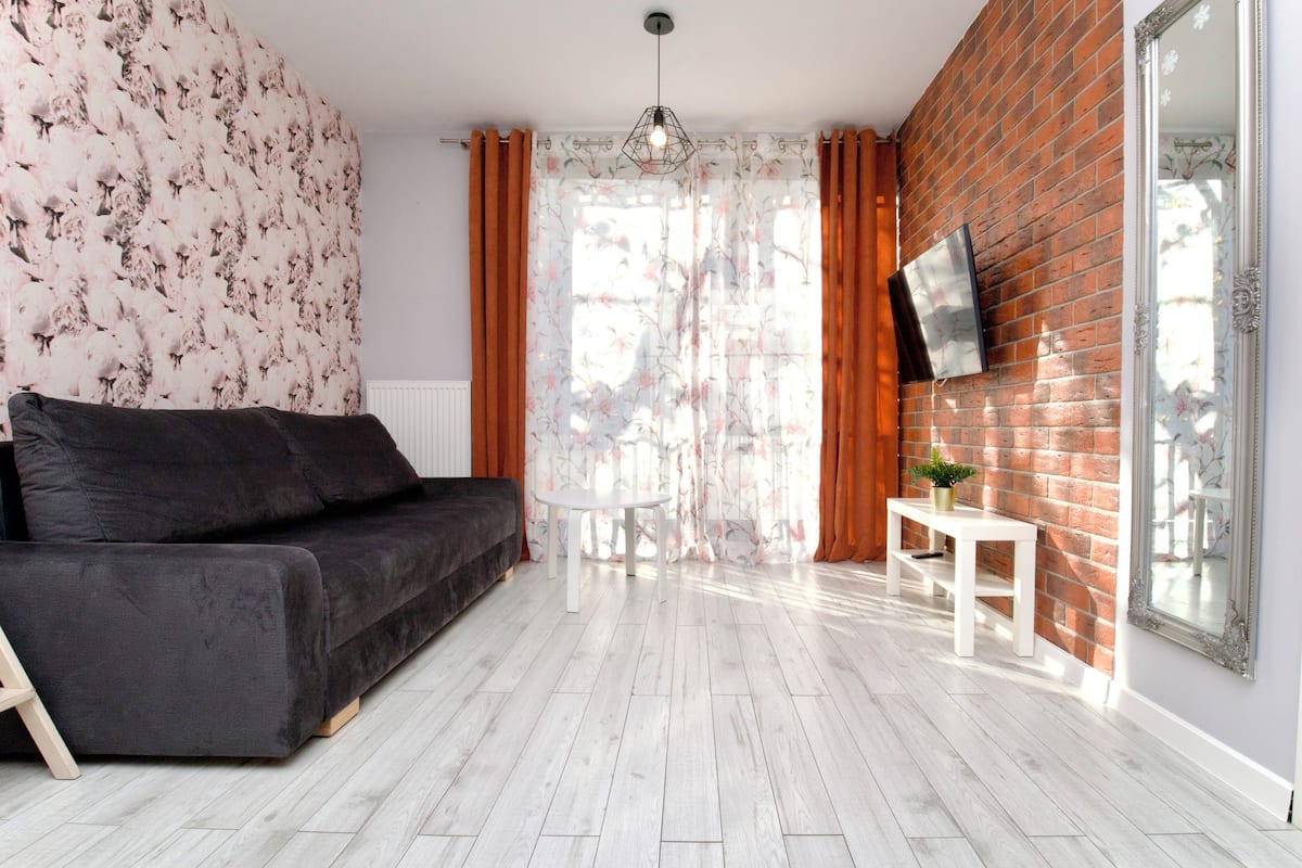 Un salon moderne avec un canapé noir, une table blanche et un mur en briques.