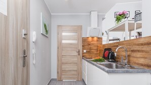 Una cocina moderna con puerta de madera, armarios blancos, pileta de acero inoxidable y horno empotrado.