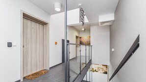 Un interior moderno con una puerta de madera, una escalera con barandillas de vidrio y una lámpara fijada a la pared.