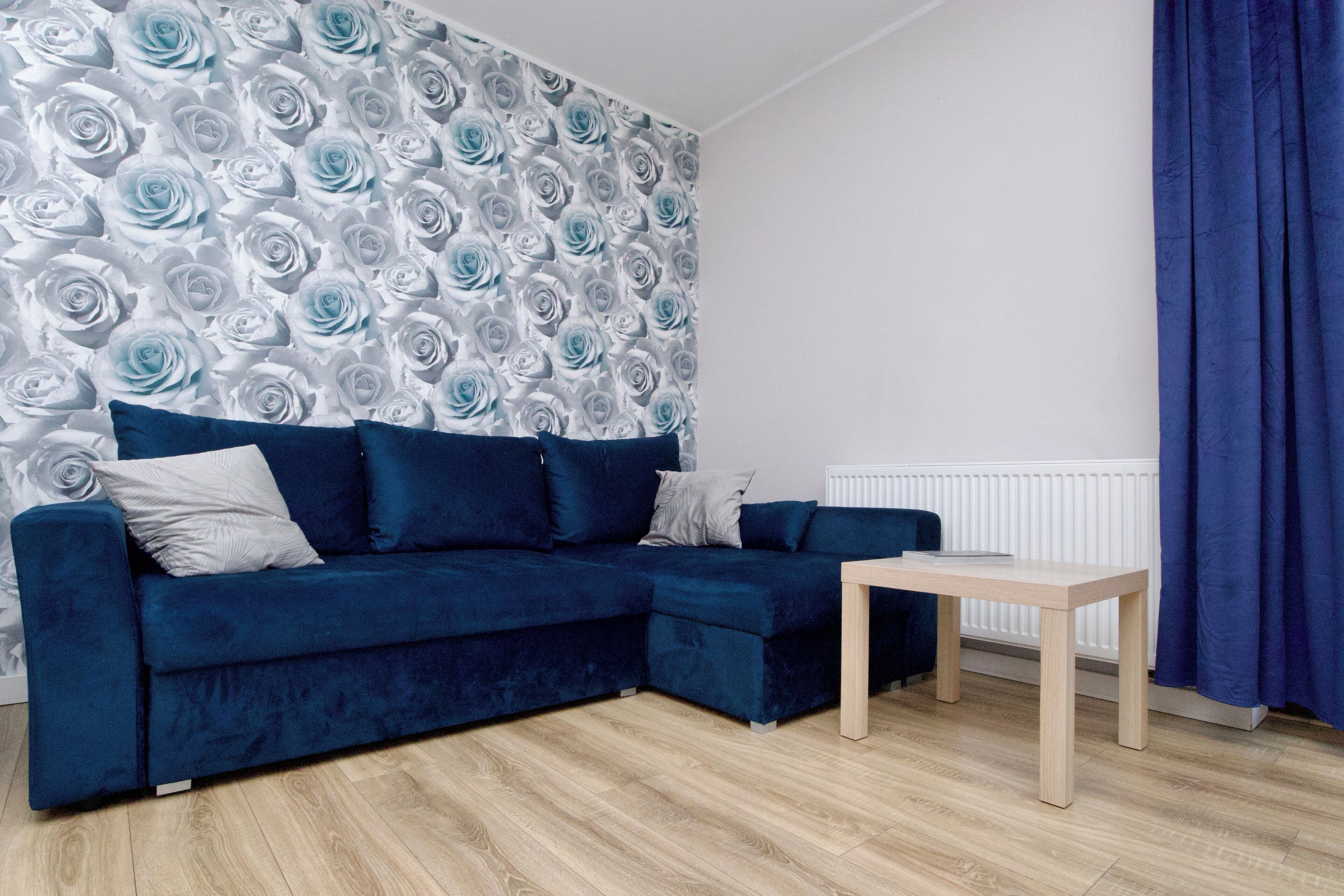 A modern living room with a blue sectional sofa, a wooden coffee table, and a patterned wallpaper.