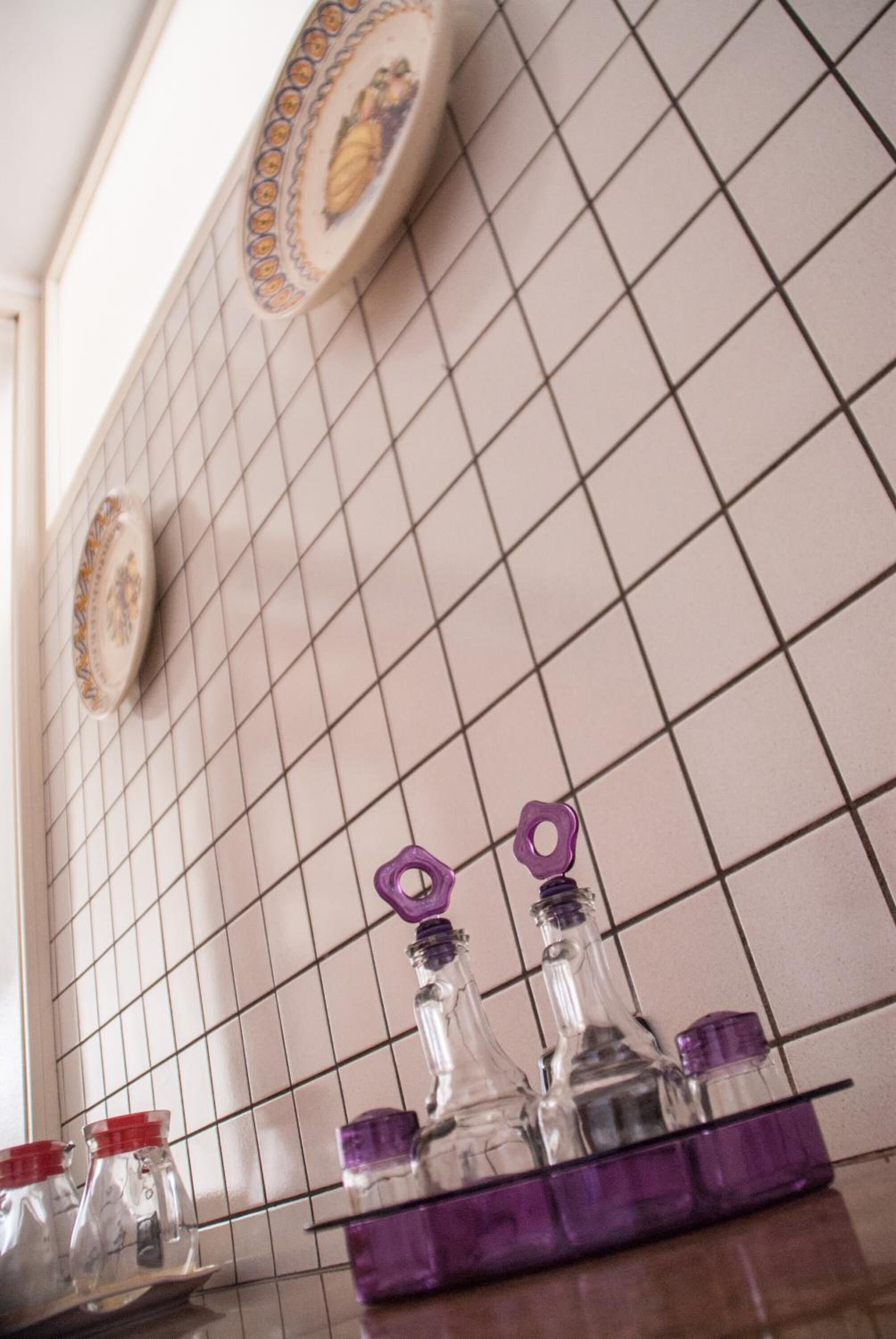 Eine Küche mit weiß gefliestem Fliesenspiegel, einem violetten Geschirrgestell und klaren Glasflaschen mit violetten Deckeln.