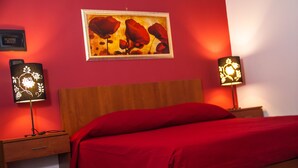 Una stanza con una testiera di legno, una coperta rossa, due lampade ai comodini e un quadro appeso alla parete.