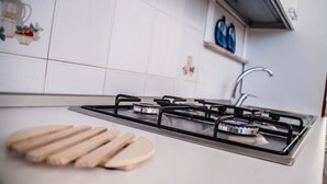 Una cucina con fornello a gas, mobili bianchi e un tagliere di legno.
