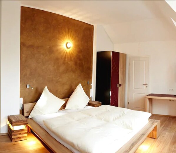 A modern bedroom with a large bed, a bedside table with a lamp, a wardrobe, and a desk with a chair.