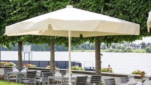 A lakeside outdoor seating area with tables and chairs under umbrellas, overlooking the water. - Residenz Schloss Engers (Neuwied)