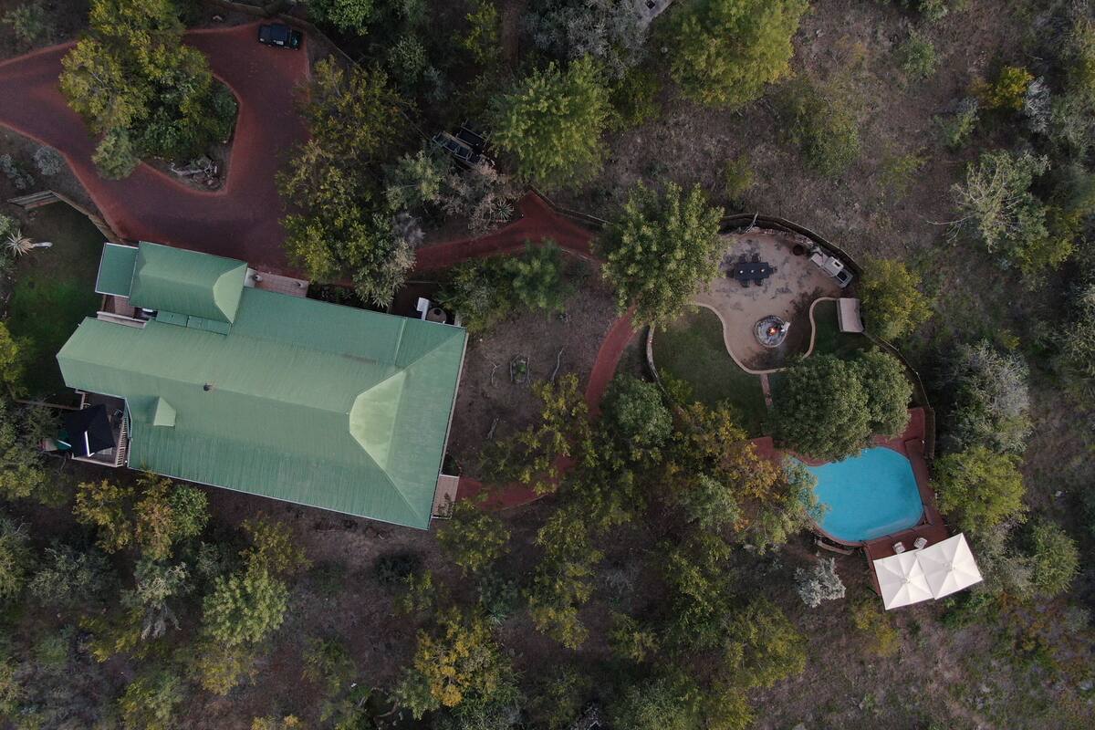 Luchtbeeld van een pand met een groot gebouw, een zwembad en een vuurplaats, omringd door bomen.