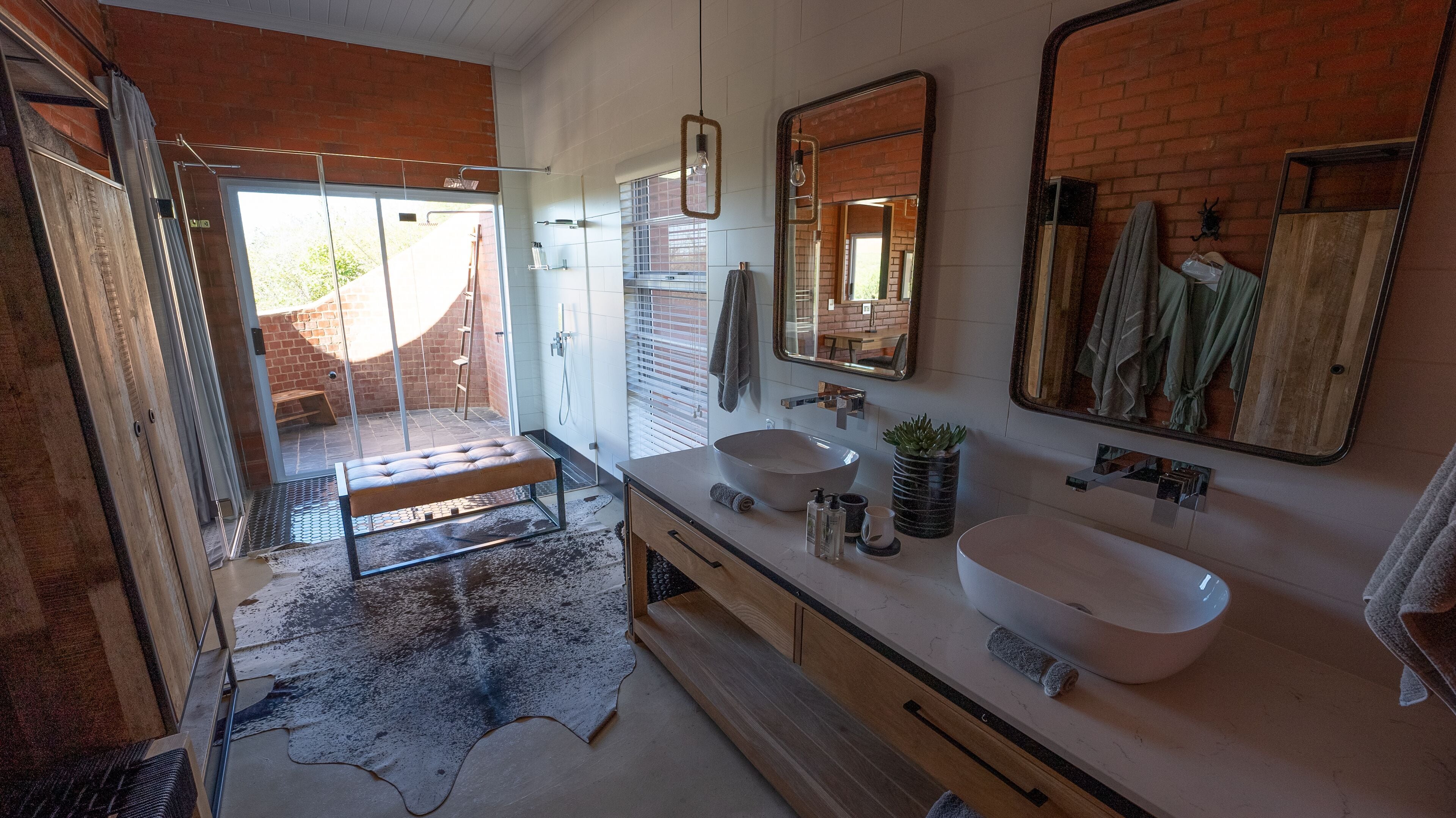A modern bathroom with a large window, a bench, two sinks, and a mirror.