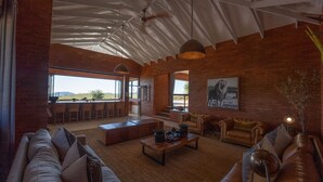 Amplia sala de estar con techo alto, barra con taburetes, ventana grande con vistas al exterior y un cuadro de león en la pared.