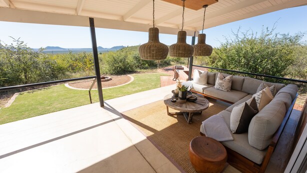 Un amplio balcón con sofá y mesa, con vistas a un jardín ajardinado y montañas lejanas.