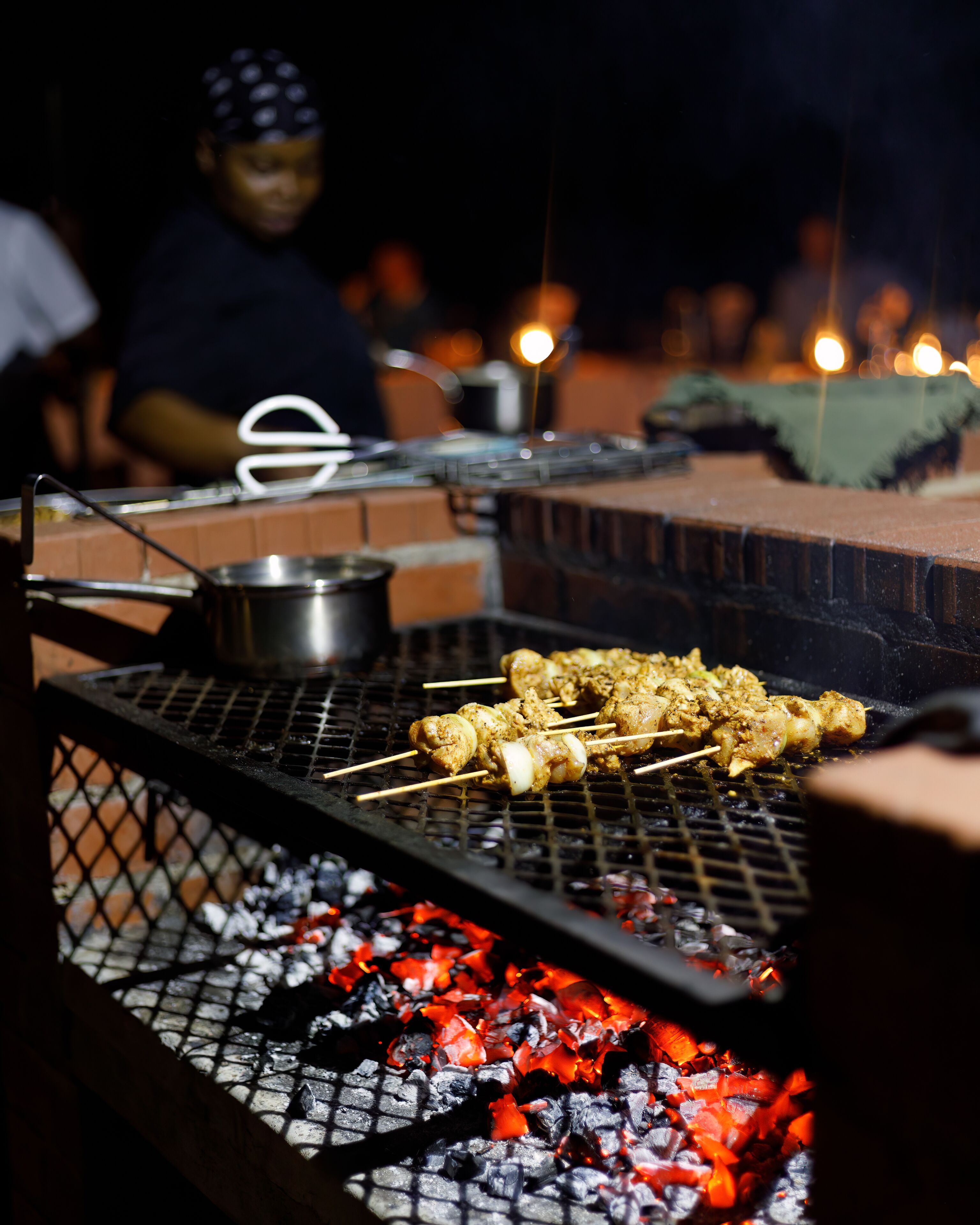 A grill with skewers of meat, charcoal, and a pot.