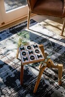 Una mesa con cubierta de vidrio y un juego de tres en raya sobre un atril de madera rústica.