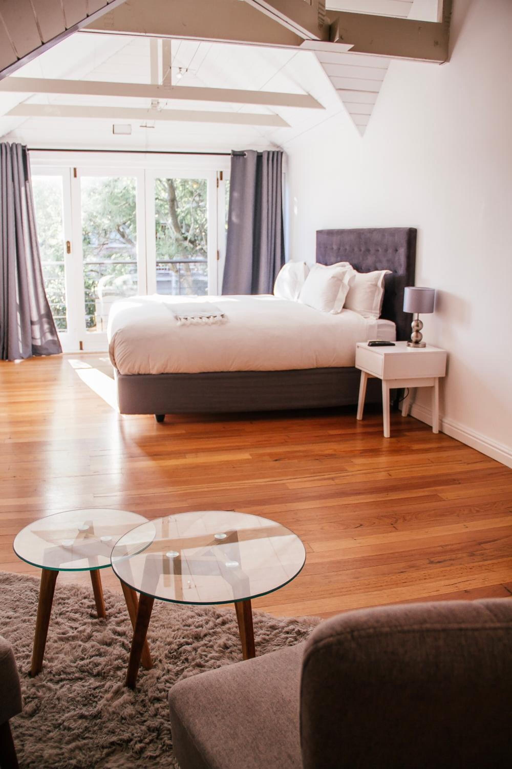 Un dormitorio con una cama grande, una mesita de noche, una mesa de vidrio y vistas al exterior.