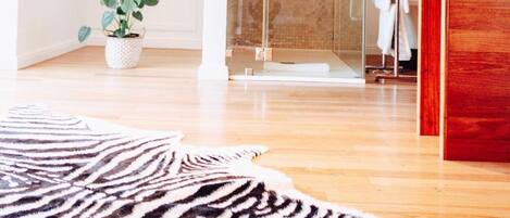 Un baño moderno con ducha de vidrio, piso de madera y alfombra estampada de cebra.