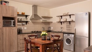 A modern kitchen with wooden cabinets, a stainless steel microwave, a built-in stove, a washing machine, and a dining area with a wooden table and chairs. - Blou Inn - Century City (Cape Town)