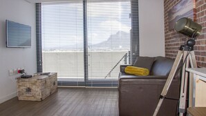 A room with a brown leather sofa, a wooden chest, and a tripod with a light. - Blou Inn - Century City (Cape Town)